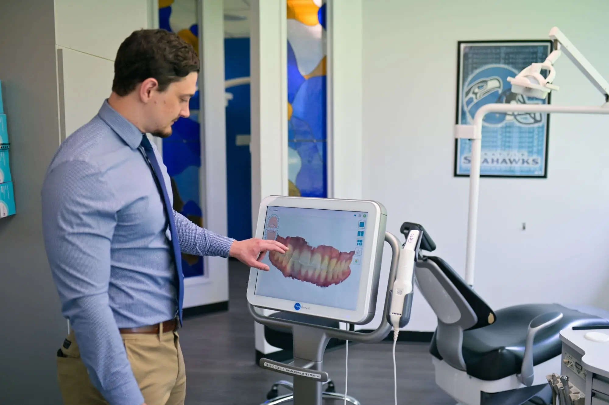 A person in a dress shirt points at an overbite visible on a dental scan displayed on a monitor in a modern dental office in Sammamish or Kent, WA