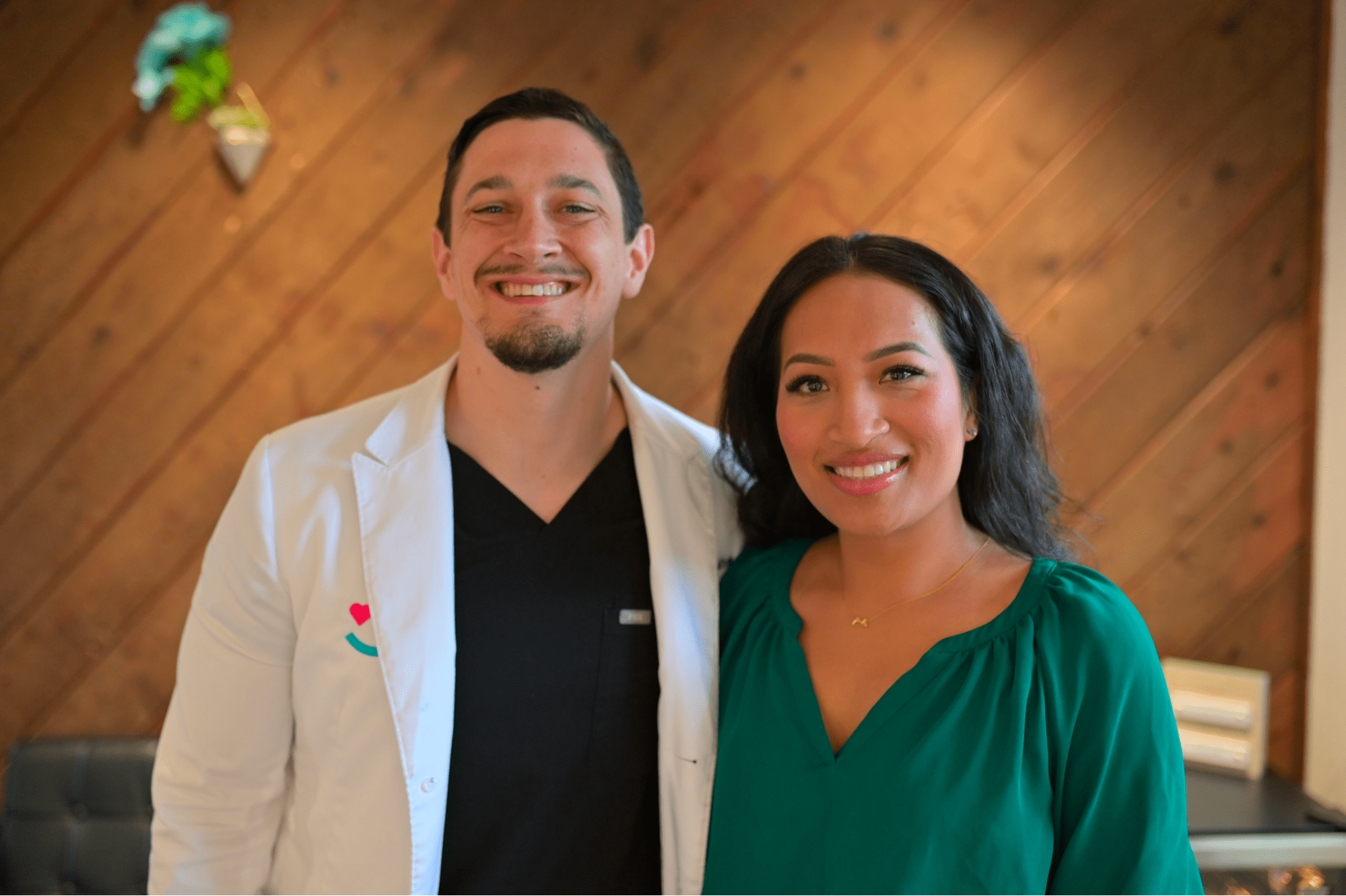 Dr. Cameron Freelove and his patient in a green blouse stand smiling before a wood-paneled wall in Sammamish, WA after a braces treatment.