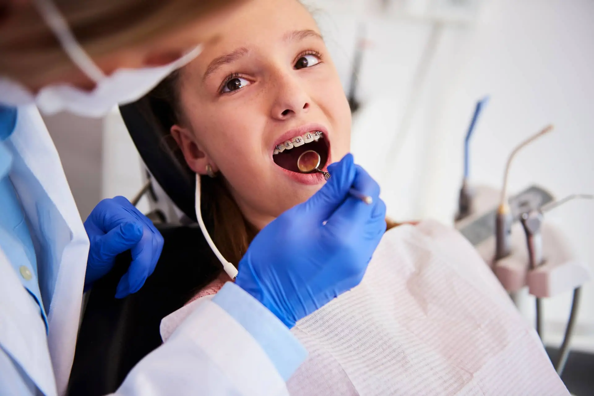 A dentist examines a patient wearing braces using a dental mirror.