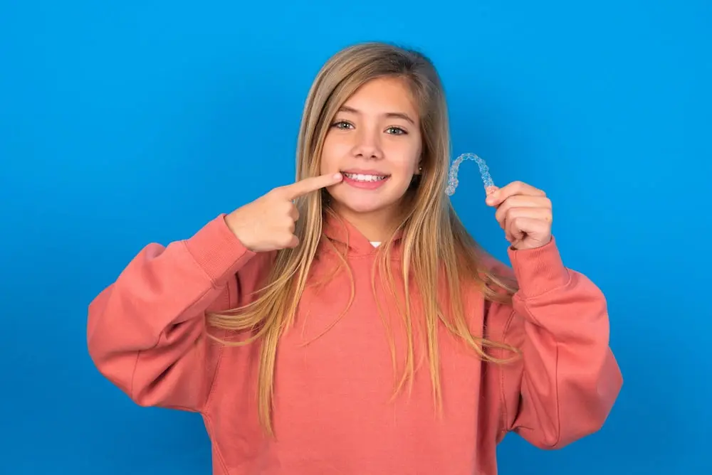A woman stands confidently, holding a Invisalign clear aligners in her hand, ready for her dental care routine as one of the Types of Braces Sammamish or Kent, WA.