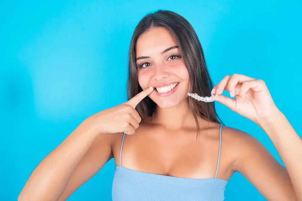 A woman pointing at her teeth, holding a Invisalign clear aligner in her hand, ready for her orthodontic care routine in Freelove Orthodontics Sammamish WA