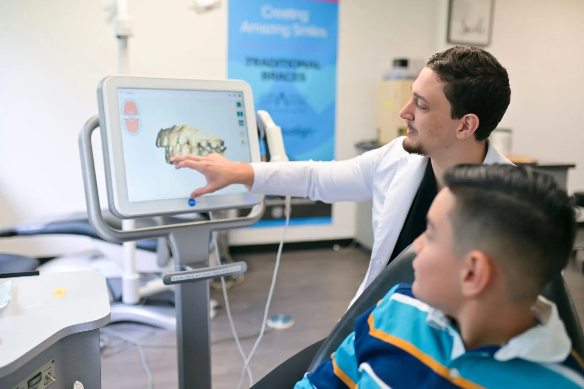 Our orthodontist, Dr. Cameron Freelove, DDS, in a white coat explains a dental scan on a monitor to a seated patient in an examination room in his office in Sammamish or Kent, WA.