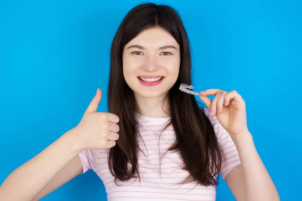 A girl stands confidently, holding a Invisalign clear aligner in her hand, ready for her orthodontic care routine in Sammamish WA