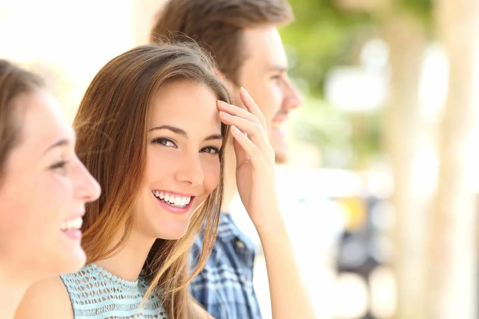 Three people stand outdoors, surrounded by the warm hues of fall. The central person, smiling directly at the camera and adjusting their hair, seems to relish the crisp air—a perfect day for testing her new Herbst appliances from an orthodontist in Sammamish or Kent, WA.