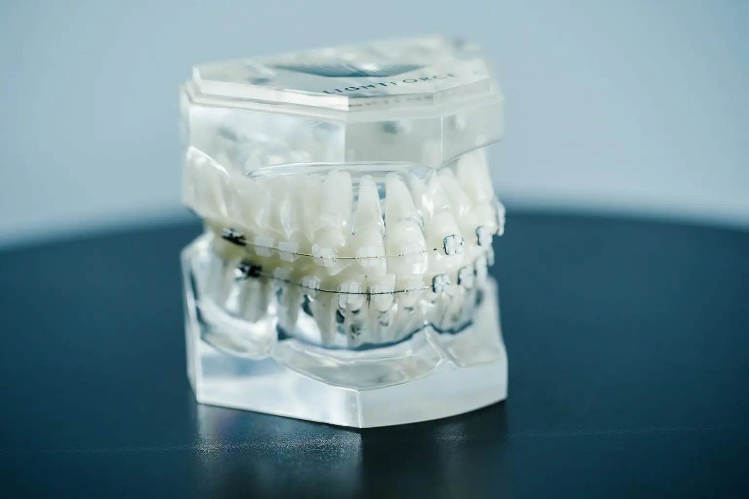 A clear dental model showcasing a set of teeth with clear braces, reminiscent of those available in Kent, WA, sits elegantly on a dark surface against a light background.