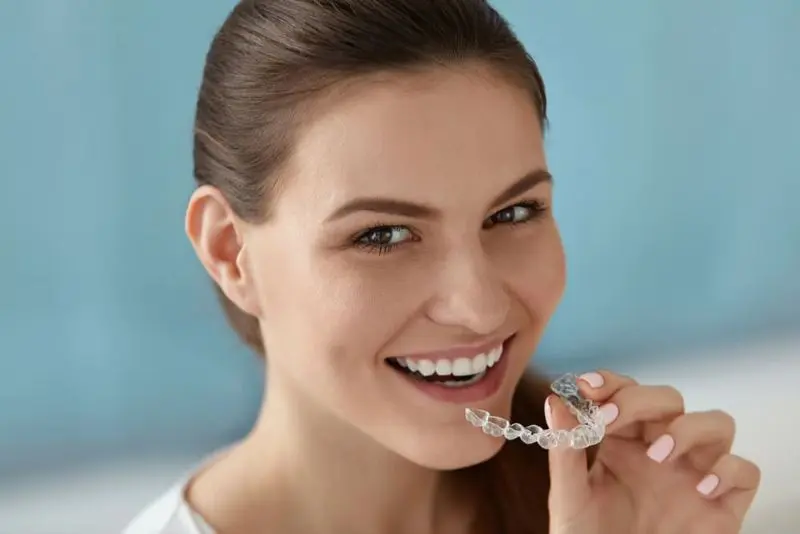 A smiling woman holds an affordable cheap Invisalign aligner near her mouth, ready to wear it in Sammamish or Kent, WA.