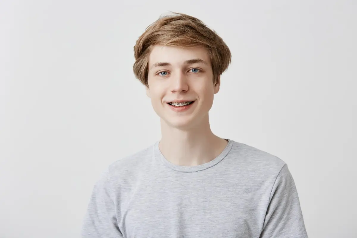 A young person with short hair and metal braces from Kent, WA, is smiling warmly in a light gray t-shirt against a plain white background.