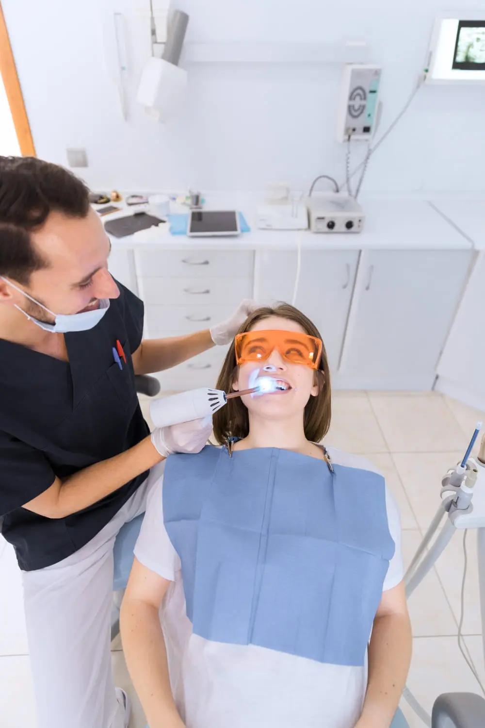 At the freelove orthodontics clinic, a dentist skillfully performs a teeth whitening procedure on a patient wearing orange protective glasses, ensuring bright and confident smiles.