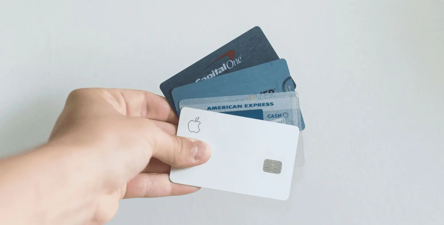 A hand holds several credit cards fanned out, including Apple, Capital One, and American Express cards, against a plain light background illustrating Invisalign Payment Plan in Sammamish or Kent, WA.