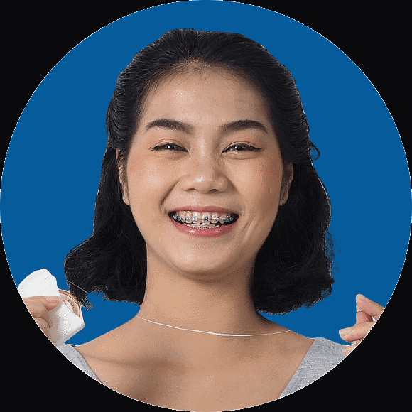 Person smiling with braces, holding dental floss against a blue background in Kent or Sammamish, WA