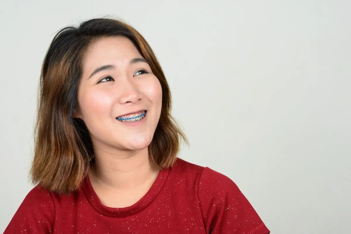 An adult with metal braces from Sammamish or Kent, WA, dressed in a red shirt, gazes upwards against a neutral background.