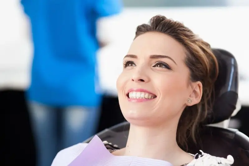 A person with brown hair and a purple dental bib smiling while sitting in a dental chair for her lingual braces (inBrace) in Sammamish or Kent, WA