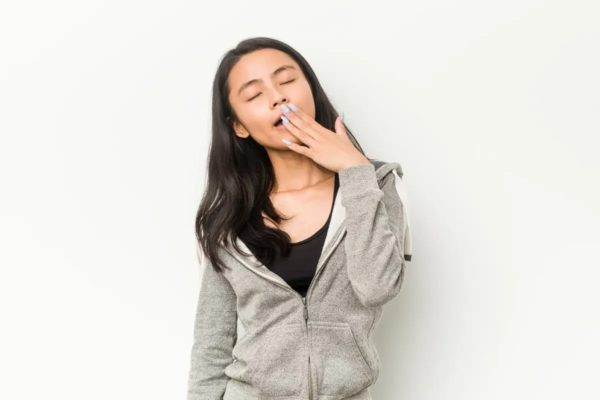 A person with long hair yawning and covering their mouth breather, wearing a gray hoodie and black shirt for orthodontist in Sammamish and Kent, WA.