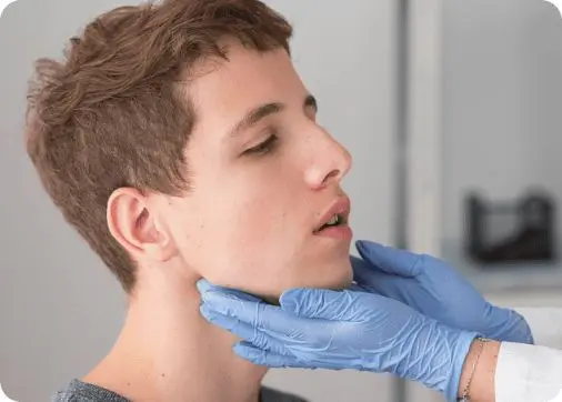 A doctor wearing blue gloves examines a young man's jaw in a clinical setting post jaw surgery.