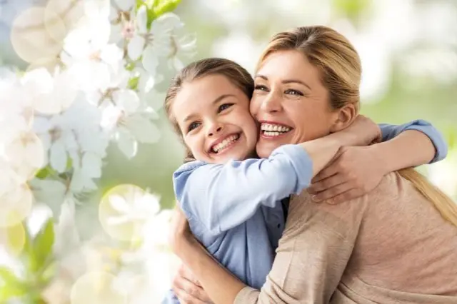 A woman and a girl, both beaming with joy, embrace in a garden adorned with white flowers. The girl's new braces add an adorable sparkle to her smile, reminding them of the smart orthodontic insurance choices in Sammamish or Kent, WA that made this moment possible.