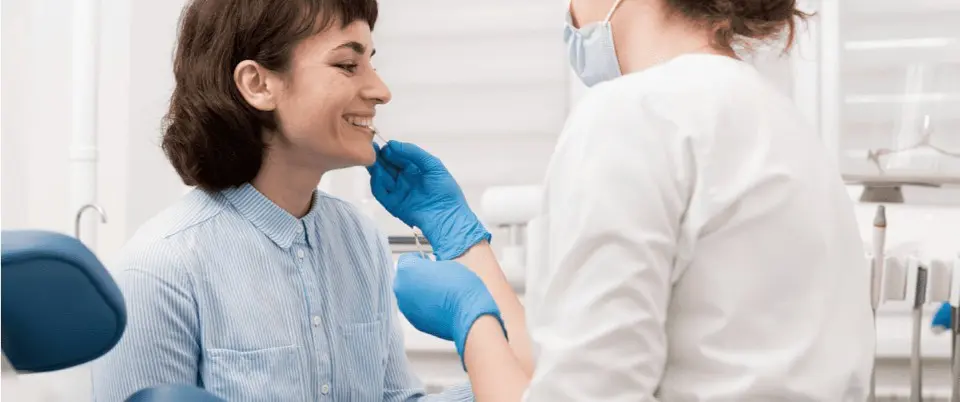 In a dental office near Sammamish or Kent, WA, an orthodontist wearing a mask and gloves carefully examines a smiling patient.