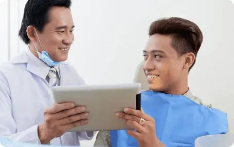 Orthodontist in Kent or Sammamish, WA showing a patient something on a tablet. The patient is seated and smiling, wearing a dental bib after a jaw surgery.