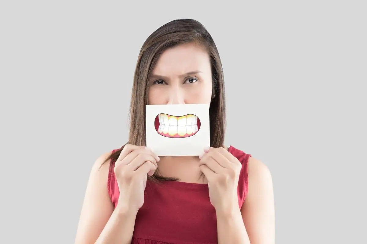 Person holding a paper with a cartoon underbite smiling mouth in front of their face, wearing a red top, against a gray background for an orthodontist in Sammamish and Kent, WA.