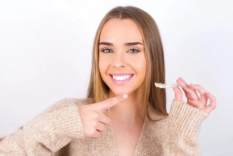 A person smiling and pointing to a dental aligner they are holding. Illustrating Invisalign Payment Plan in Sammamish or Kent, WA