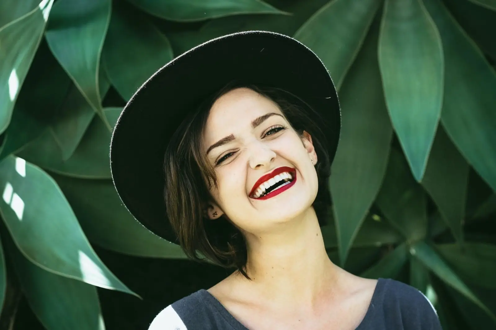 A person in a wide-brimmed hat smiles in front of large green leaves near orthodontist in Sammamish or Kent, WA.