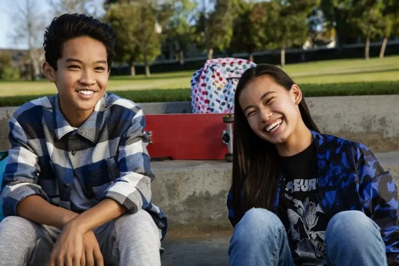 Two teenagers sitting outdoors on concrete steps, smiling confidently with their Invisalign aligners. A skateboard and a polka-dot backpack are placed behind them, hinting at an afternoon of adventure and carefree fun. Illustrating Invisalign insurance in Sammamish or Kent, WA.