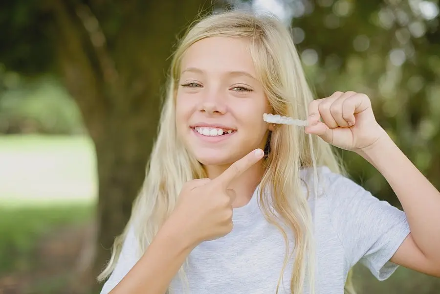 Girl with long blonde hair smiling and pointing at a dental aligner she's holding in her hand in Sammamish or Kent, WA.