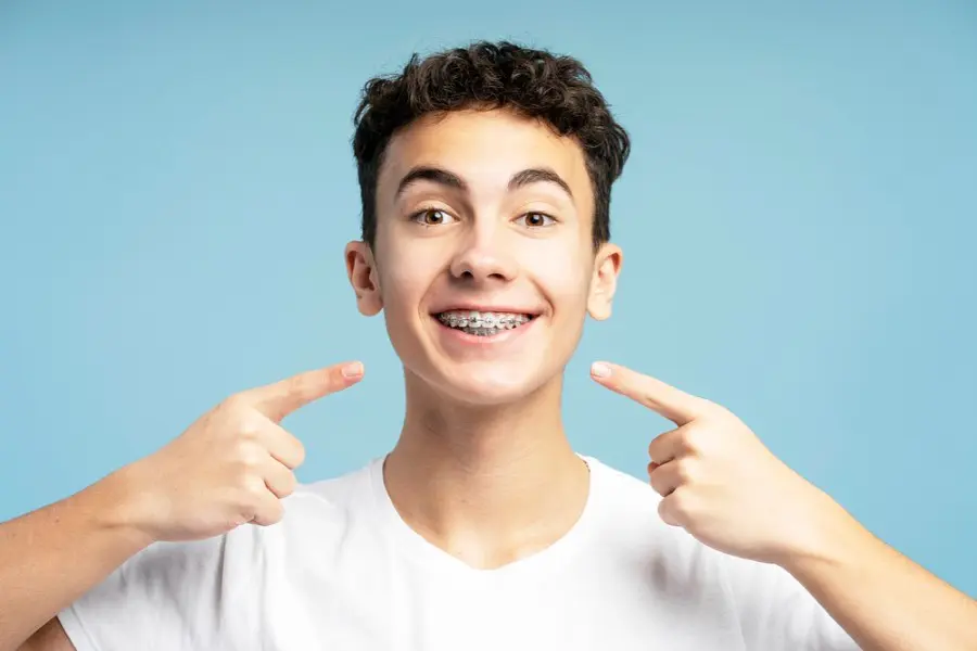 A smiling young person with curly hair points to their braces, wearing a white shirt in Sammamish or Kent, WA.