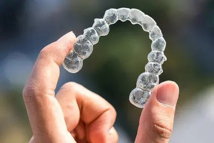 A hand gently cradles an Invisalign clear aligner against a beautifully blurred backdrop, capturing the essence of dental precision in Kent, WA.