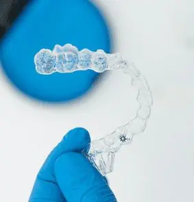A gloved hand holds a transparent dental aligner against a blurred background. Illustrating Invisalign Payment Plan in Sammamish or Kent, WA