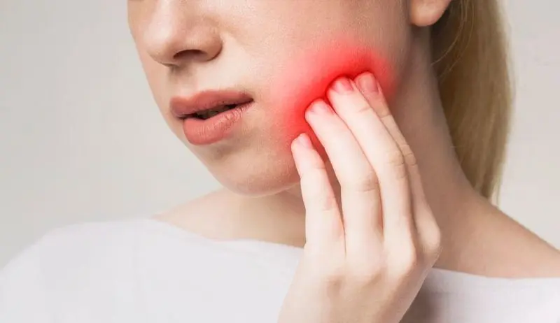 Person holding their cheek with a red glow, indicating pain or toothache. Illustrating Invisalign vs braces in Sammamish or Kent, WA.