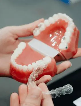 Hands holding a dental model of teeth with a clear aligner in the foreground. Illustrating Invisalign Payment Plan in Sammamish or Kent, WA